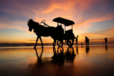 Silhouette people riding horse on beach against sky during sunset