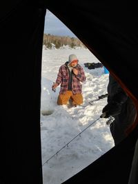 Man kneeling on snow covered field seen through tent