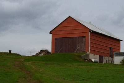 Barn on grassy field against cloudy sky