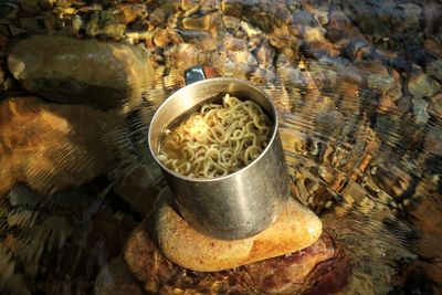 Close up of noodles in a mug on a rock in a river