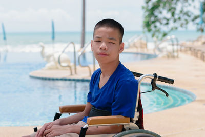 Portrait of boy sitting on wheelchair against swimming pool