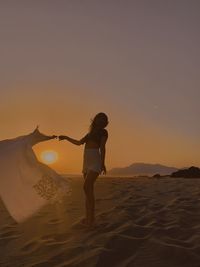 Woman on beach against sky during sunset