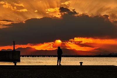 Silhouette man standing on beach against sky during sunset