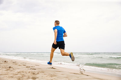 Rear view of man running on beach against sky