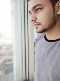 Young man looking through window at home