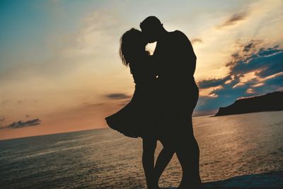 Silhouette couple on beach against sky during sunset