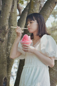 Midsection of woman holding ice cream standing by tree