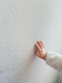 Cropped child touching white wall at home