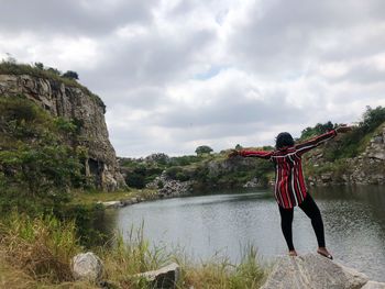 Rear view of woman with arms outstretched standing on rock at lake