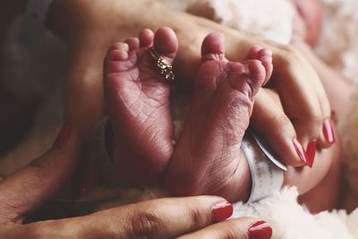 Cropped hands of mother holding newborn feet on bed