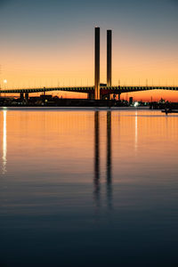 Scenic view of river by illuminated buildings against sky during sunset