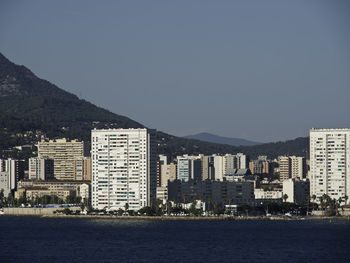 Buildings by sea against clear sky in city