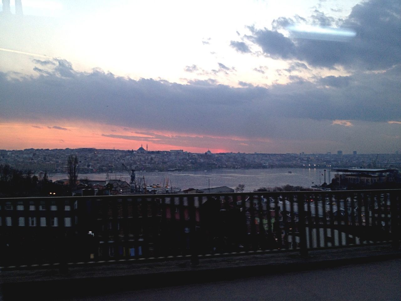 sunset, sky, railing, built structure, architecture, cloud - sky, building exterior, water, orange color, city, sea, nature, cityscape, cloud, high angle view, river, outdoors, silhouette, sun, scenics