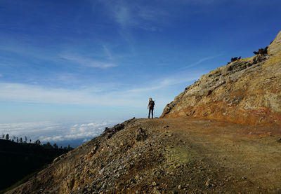 Rear view of woman standing on dirt road against sky