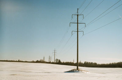 Electricity pylons on snow covered landscape against sky