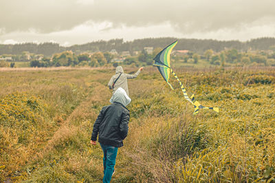 Rear view of kid with mother playing with toy on meadow against sky