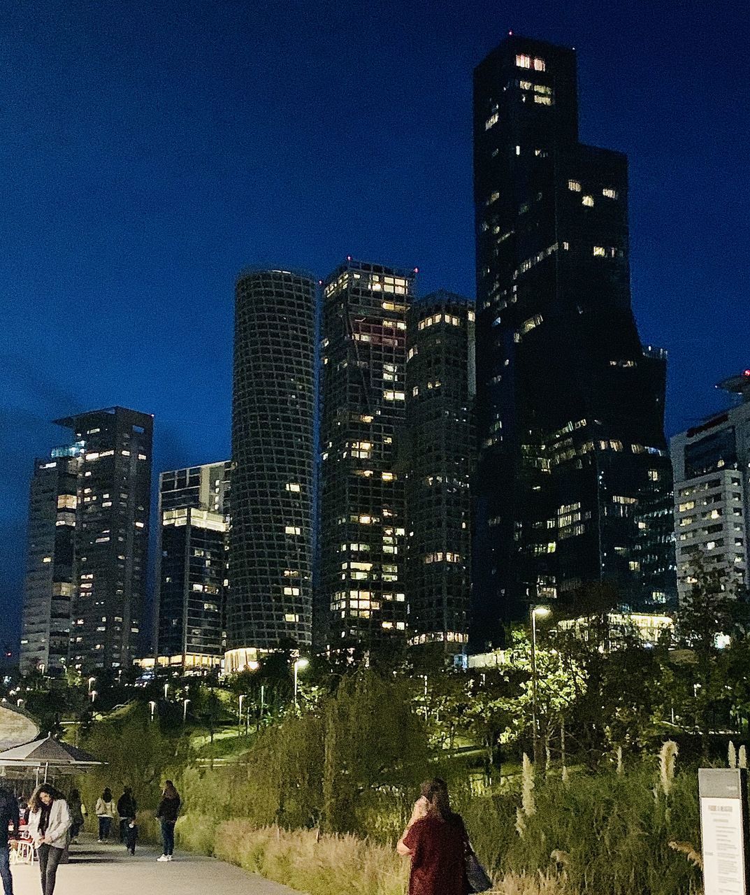 PEOPLE ON ILLUMINATED MODERN BUILDINGS AGAINST SKY IN CITY