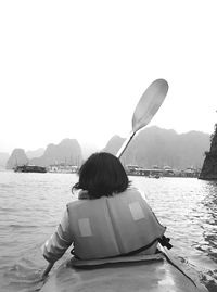 Rear view of boy sitting on boat in lake against clear sky