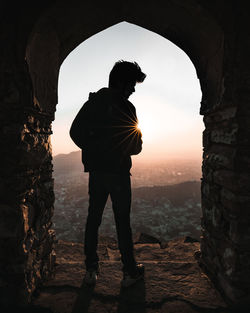 Rear view of silhouette man standing by entrance against sky during sunset