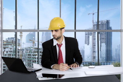 Architect wearing suit and yellow hardhat working in office