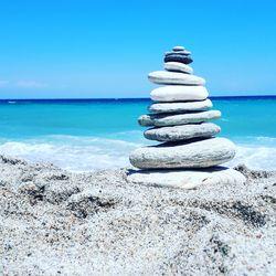 Stack of pebbles on beach against clear blue sky