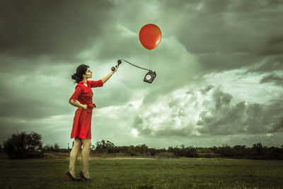 Woman standing with balloons on field against cloudy sky