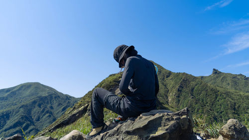 Rear view of man sitting on rock against sky