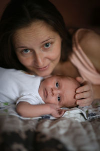 Portrait of smiling boy lying on bed at home with mother 