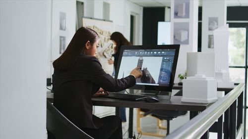 Side view of woman using laptop while standing in office