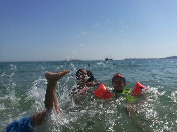 Young man splashing water in sea against sky