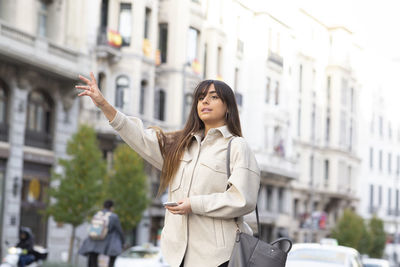 Young woman using phone while standing on street in city