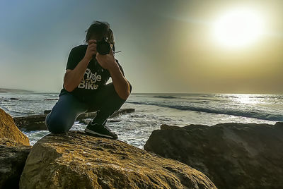 Woman standing on rock by sea against sky