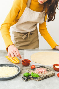Caucasian girl in an apron at the table with ingredients and dough mixes the sauce for making pizza 