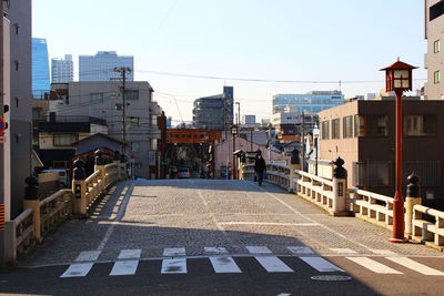 Road by buildings against clear sky in city