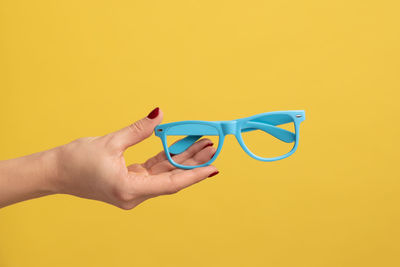 Cropped hand holding sunglasses against green background