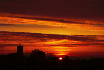 Silhouette buildings against dramatic sky during sunset