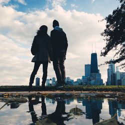 Rear view of man and woman looking at cityscape against cloudy sky