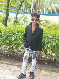 Portrait of young woman wearing sunglasses standing against plants