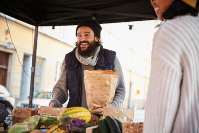 Smiling man buying vegetables from female vendor at market stall