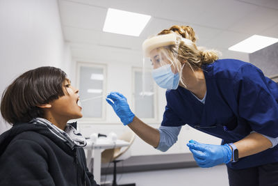 Female doctor performing covid-19 swab test on boy patient