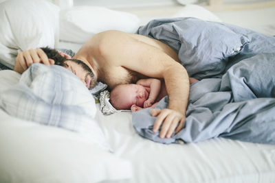 Man with newborn baby sleeping in bed