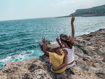 Rear view of mother and son gesturing peace sign while sitting at beach