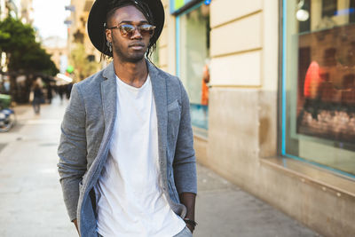 Fashionable young man in hat standing at city