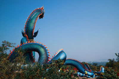 Low angle view of dragon statue against clear blue sky
