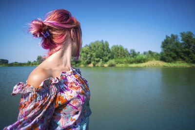 Woman with dyed hair standing in lake against clear sky