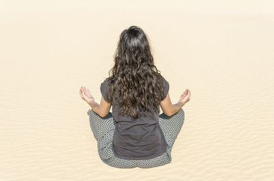 Rear view of woman sitting on sand