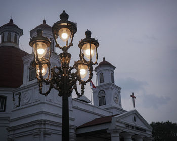 Low angle view of illuminated street light by building against sky