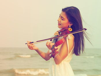 Woman playing violin by sea against clear sky