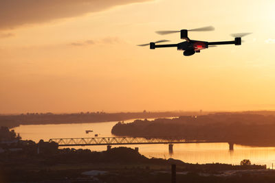 Silhouette airplane flying over river against sky during sunset