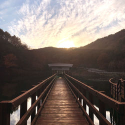 Footbridge over river against sky during sunset